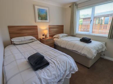 A bedroom with two single beds a nightstand lamp and a window at Wansfell Retreat Lodge Wansfell 4 Limefitt Park near Windermere