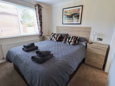 A bedroom with a double bed covered with a gray quilt and matching towels a wooden headboard two bedside tables with lamps and a framed picture on the wall at Wansfell Retreat Lodge Wansfell 4 Limefitt Park near Windermere