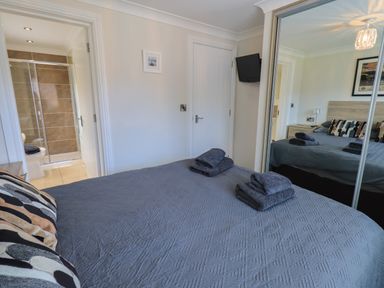 A bedroom with a bed covered by a gray quilt and folded towels a mirrored wardrobe a door leading to a bathroom and a wall-mounted television at Wansfell Retreat Lodge Wansfell 4 Limefitt Park near Windermere
