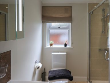 A bathroom with a toilet, shower enclosure, window with a blind, toilet paper holder, and items on the windowsill at Wansfell Retreat Lodge Wansfell 4 Limefitt Park near Windermere