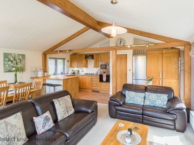 An open plan living room and kitchen with leather sofas a wooden dining table and kitchen cabinets at Sheffield Pike Lodge Ullswater 8 Limefitt Park near Windermere