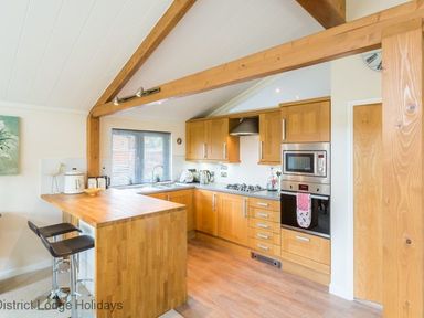A kitchen with wooden cabinets and a breakfast bar with stools at Sheffield Pike Lodge Ullswater 8 Limefitt Park near Windermere