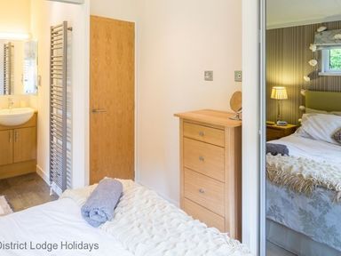 A bedroom with a wooden chest of drawers a bed with a white blanket and a rolled towel and an en suite bathroom at District Lodge Holidays