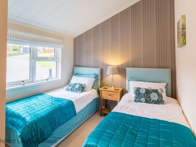 A bedroom with two single beds with turquoise bedding and a wooden bedside table with a lamp between them at Sheffield Pike Lodge Ullswater 8 Limefitt Park near Windermere