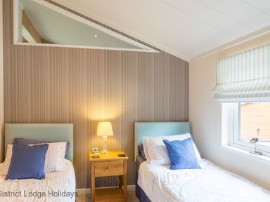 A bedroom with two single beds separated by a wooden nightstand with a lamp and a window on the right at Sheffield Pike Lodge Ullswater 8 Limefitt Park near Windermere