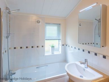 A bathroom with a bathtub shower basin mirror window and a small plant at Sheffield Pike Lodge Ullswater 8 Limefitt Park near Windermere