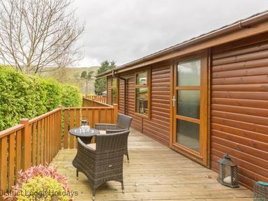 A wooden deck with two wicker chairs and a round table outside a wooden lodge at Sheffield Pike Lodge Ullswater 8 Limefitt Park near Windermere