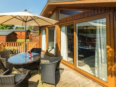 An outdoor patio with a table umbrella chairs and wooden deck at Sheffield Pike Lodge Ullswater 8 Limefitt Park near Windermere