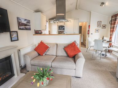 A living room with a sofa and flower vase and a dining area at Shoreside Lodge L8 Fallbarrow Park near Bowness on Windermere