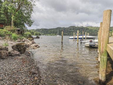 A lakeshore with boats docked and a forested hillside in the background at Shoreside Lodge in L8 Fallbarrow Park near Bowness on Windermere