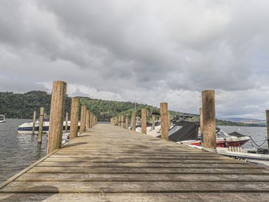 A wooden dock extending into a lake with boats moored on either side and trees in the background at Shoreside Lodge in L8 Fallbarrow Park near Bowness on Windermere