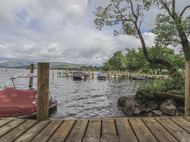 A wooden dock on a lake with covered boats and trees at Shoreside Lodge in L8 Fallbarrow Park near Bowness on Windermere