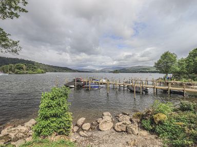 A lakeside view with wooden docks and boats tied up at Shoreside Lodge L8 Fallbarrow Park near Bowness on Windermere