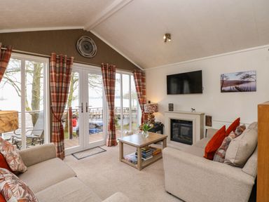 A living room with sofas coffee table fireplace and large windows overlooking a lake at Shoreside Lodge in L8 Fallbarrow Park near Bowness on Windermere