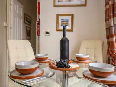 A dining table with four place settings and a bottle and a plate of grapes and cheese in a dining room at Shoreside Lodge L8 Fallbarrow Park near Bowness on Windermere