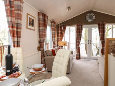 A living room with beige sofas and red plaid curtains overlooking a lake at Shoreside Lodge L8 Fallbarrow Park near Bowness on Windermere