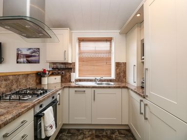 A kitchen with a gas stove oven cabinets a sink and a window with blinds at Shoreside Lodge in L8 Fallbarrow Park near Bowness on Windermere