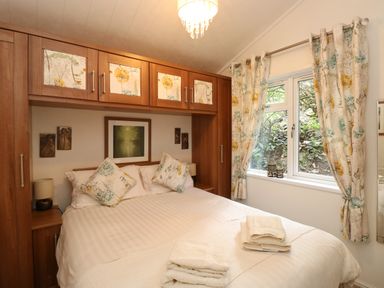 A bedroom with a double bed cushions curtains and built in wooden wardrobes at Shoreside Lodge L8 Fallbarrow Park near Bowness on Windermere