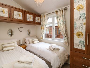 A bedroom with two single beds and floral curtains at Shoreside Lodge L8 Fallbarrow Park near Bowness on Windermere