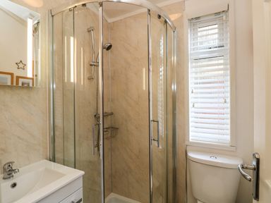 A bathroom with a corner glass shower enclosure a white sink and a toilet with a window with blinds at Shoreside Lodge in L8 Fallbarrow Park near Bowness on Windermere