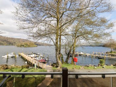 A view of a lake with boats docked at wooden piers and trees along the shore at Shoreside Lodge L8 Fallbarrow Park near Bowness on Windermere