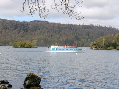 A boat on a lake with forested hills in the background at Shoreside Lodge L8 Fallbarrow Park near Bowness on Windermere