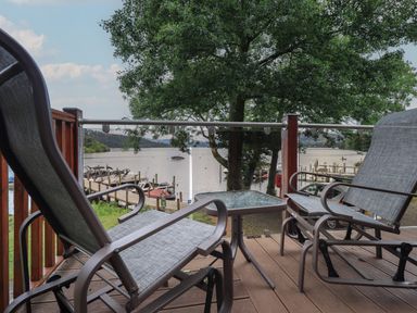 A balcony with two chairs and a small table overlooking a lake with boats and trees at Shoreside Lodge L8 Fallbarrow Park near Bowness on Windermere