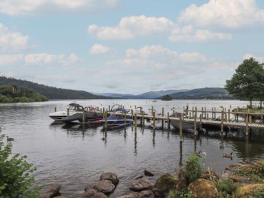 A dock with boats on a lake surrounded by hills and trees at Shoreside Lodge L8 Fallbarrow Park near Bowness on Windermere