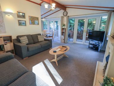 A living room with two sofas a coffee table a television and double glass doors opening to a balcony at Walkers Retreat Lodge in Fellside 5 Limefitt Park near Windermere