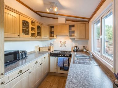 A kitchen with wooden cabinets a stove a microwave kettle toaster and a sink under a window at Walkers Retreat Lodge Fellside 5 Limefitt Park near Windermere