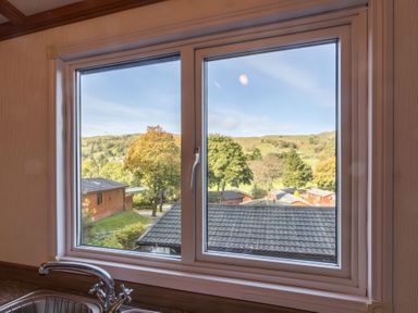 A kitchen sink with a faucet under a window showing rooftops trees and hills at Walkers Retreat Lodge Fellside 5 Limefitt Park near Windermere