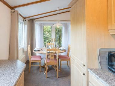 A dining area with a round wooden table and four chairs near glass doors at Walkers Retreat Lodge Fellside 5 Limefitt Park near Windermere