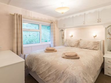 A bedroom with a double bed, bedside tables, overhead cabinets, and a window with curtains at Walkers Retreat Lodge in Fellside 5 Limefitt Park near Windermere
