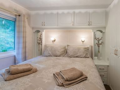 A bedroom with a double bed towels on the bed bedside tables with lamps and vases and window with curtains at Walkers Retreat Lodge Fellside 5 Limefitt Park near Windermere