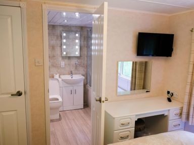 A bedroom with a desk and mounted TV next to a door open to a bathroom with toilet sink and mirror at Walkers Retreat Lodge Fellside 5 Limefitt Park near Windermere