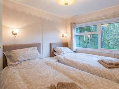 A bedroom with two single beds side by side with patterned bedding and window showing trees outside at Walkers Retreat Lodge Fellside 5 Limefitt Park near Windermere