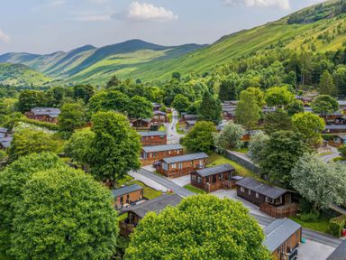 A cluster of wooden lodges surrounded by trees and green hills at Walkers Retreat Lodge Fellside 5 Limefitt Park near Windermere