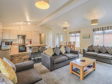 A living room with three sofas a wooden coffee table and a dining table next to an open kitchen at Daffodils Lodge Oakside 7 Fallbarrow Park in Bowness on Windermere