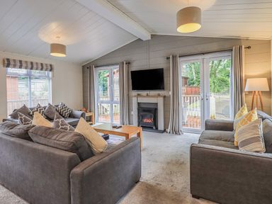 A living room with two gray sofas a wooden coffee table a wall-mounted TV and a fireplace at Daffodils Lodge Oakside 7 Fallbarrow Park in Bowness on Windermere