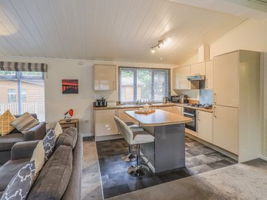 A kitchen and living area with a kitchen island and two stools at Daffodils Lodge Oakside 7 Fallbarrow Park in Bowness on Windermere