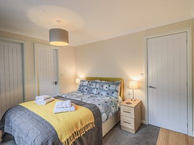 A bedroom with a bed made with patterned bedding and towels on top next to a nightstand with a lamp at Daffodils Lodge Oakside 7 Fallbarrow Park in Bowness on Windermere