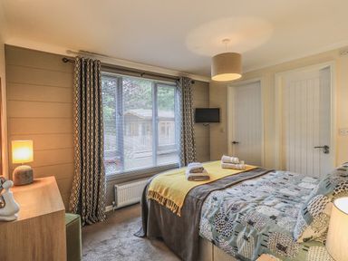 A bedroom with a bed towels on bed a window with blinds and curtains and two white doors at Daffodils Lodge Oakside 7 Fallbarrow Park in Bowness on Windermere