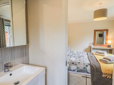 A bathroom sink next to a bedroom with a bed a mirror a lamp and folded towels at Daffodils Lodge Oakside 7 Fallbarrow Park in Bowness on Windermere