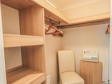 A walk in closet with wooden shelves hangers and a beige chair at Daffodils Lodge Oakside 7 Fallbarrow Park in Bowness on Windermere