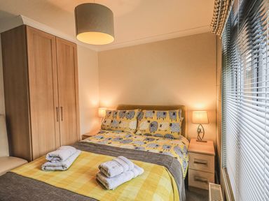 A bedroom with a bed with patterned bedding and towels on it a wardrobe and bedside tables with lamps at Daffodils Lodge Oakside 7 Fallbarrow Park in Bowness on Windermere