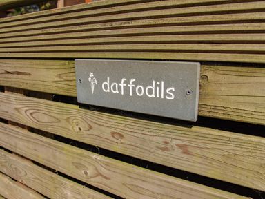 A wooden fence with a grey sign reading daffodils with a flower icon at Daffodils Lodge Oakside 7 Fallbarrow Park in Bowness on Windermere