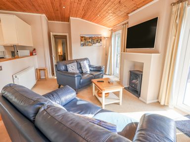 A living room with two leather sofas a wooden coffee table a wall-mounted television and a fireplace at Tanglewood Lodge Thirlmere 15 White Cross Bay near Windermere