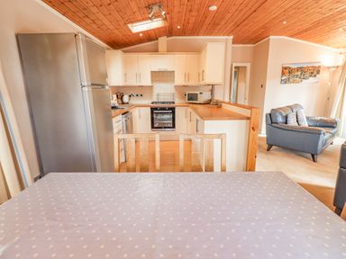 A kitchen with white cabinets stainless steel refrigerator and a dining table with wooden chairs at Tanglewood Lodge in Thirlmere 15 White Cross Bay near Windermere