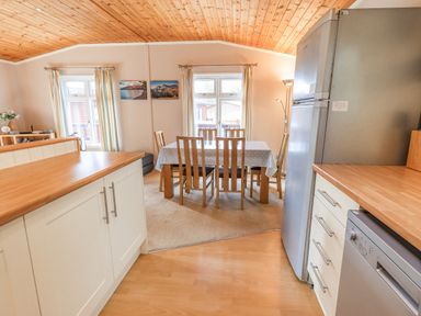 A kitchen area with wooden countertops and white cabinets next to a dining table with six wooden chairs at Tanglewood Lodge in Thirlmere 15 White Cross Bay near Windermere
