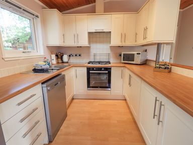 A kitchen with white cabinets wooden countertops dishwasher oven microwave and a window at Tanglewood Lodge in Thirlmere 15 White Cross Bay near Windermere
